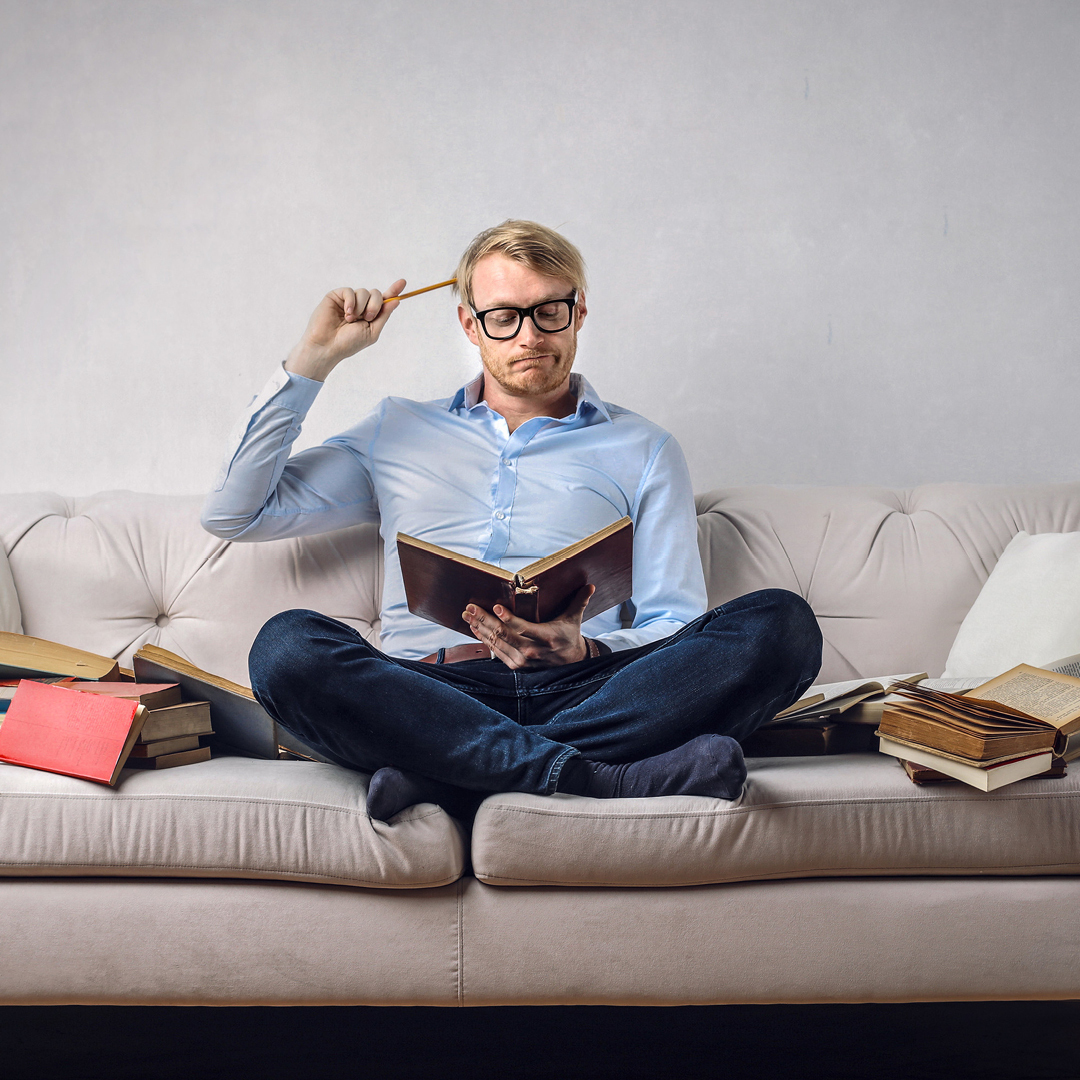 Mann sitzt auf Couch und liest ein Buch.