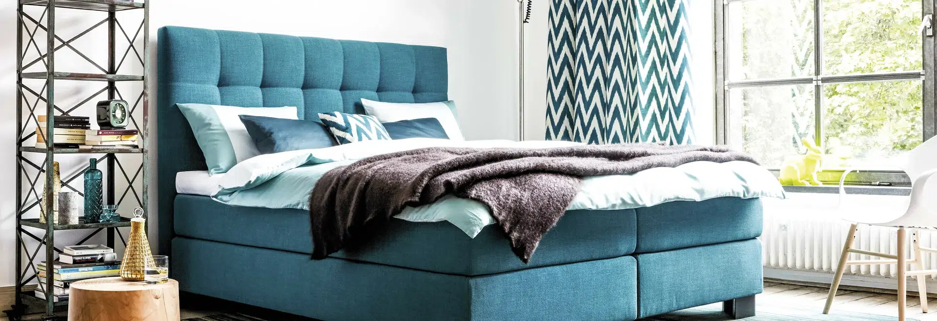 Modernes blaugrünes Boxspringbett mit Kissen und Decke.